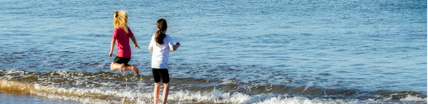 Unleash your potential Two children playing by the seaside, splashing in gentle waves, showcasing ART Excel life skills.